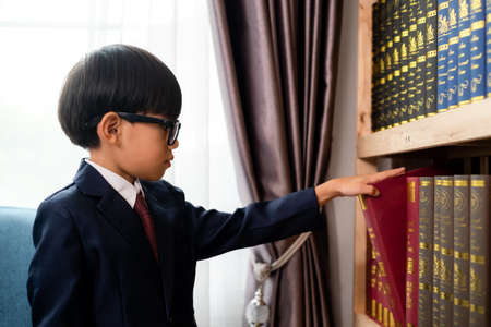 Little boys in suit looking and choose book in shelf.