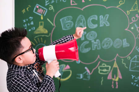 little boy in casual dress having fun with megaphone on blackboard.