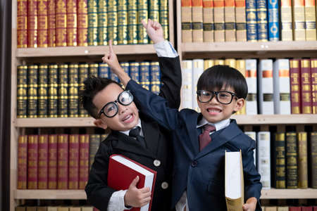 Little boys in suit looking and choose book in shelf.の写真素材