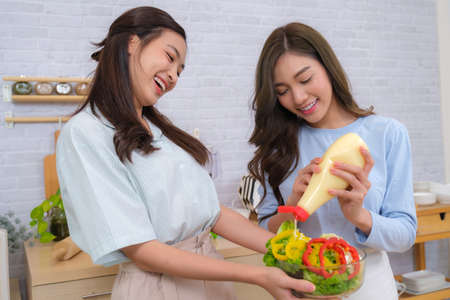 Young Asian couple women enjoy to cooking salad at home.の写真素材