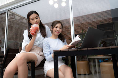Young Asian couple relaxing in bed reading a book and using a laptop to shop onlineの写真素材