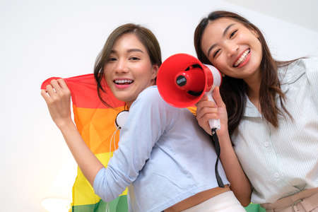 Young Asian couple relaxing in bed reading a book and using a laptop to shop online