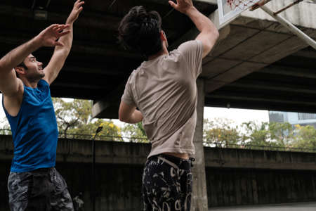 Two caucasian men pratice baskegball in court at urban street.