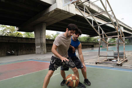 Two caucasian men pratice baskegball in court at urban street.