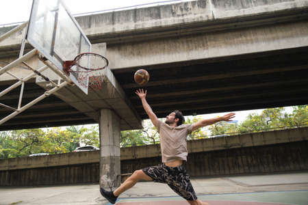 Young causian basketball player shooting ball on street court.