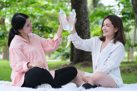 Pregnant woman with her friends  drinking water in the park.