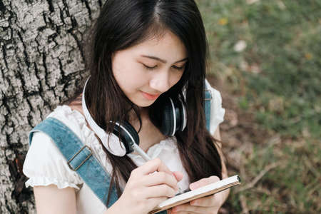 Young Asian teenage girl learning online with tablet and notebook in park.の写真素材