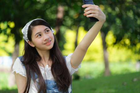 Young Asian teenage relaxing in park and she using mobile to post on scial media.の写真素材