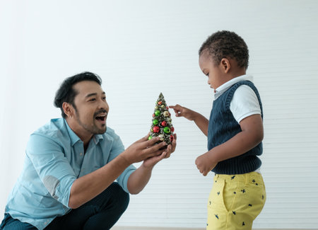 Daddy and son enjoy using times to decrorate christmas tree and take a selfie with mobile at home.