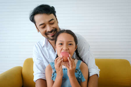 Asian happy family. Father looking his daughter eating apple and very happy.の写真素材