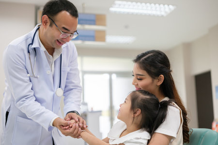 The doctor held the young patient's hand, and the mother smiled and encouraged her.の写真素材