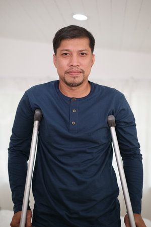 Asian man using Crutches Because he is infury at knee at home.