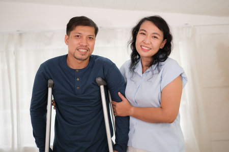 Happy Asian family  spending time at home. A wife with prosthetic leg and husban hurt a knee, Their takecare each other and relaxing at home.の写真素材