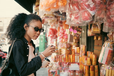 Asian woman enjoy travel in  downtown district and she taking a photo and using mobile live on social media and tasting streetfoods.の写真素材