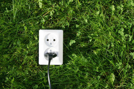 An electrical cord connected to an electrical socket that generates power from green grass or other relevant natural sources of energyの写真素材