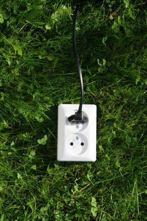 An electrical cord connected to an electrical socket that generates power from green grass or other relevant natural sources of energyの写真素材