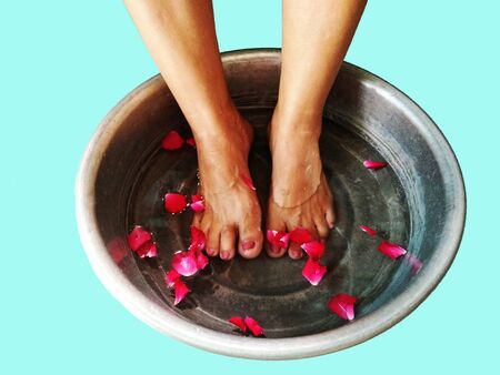 Female feet soak in water with petals of red rose in aluminum basin on blue backgroundの写真素材