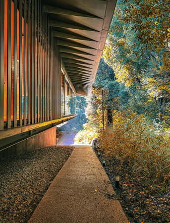 Pathway beneath a wooden building, bathed in sunlight amidst a natural garden.