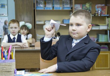 Russia, Krasnoyarsk region, Igarka, December 2015: back to school, boy launches paper plane sitting at school Deskのeditorial素材