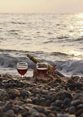 Ripe pomegranate fruit with a glass of wine and a bottle on the beach. Romantic day at the seaside. Waves and sea in the background. on the shore lay the yellowed leaves. The concept of the wedding or the celebration of Valentine day.の写真素材