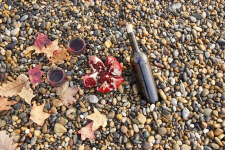 Ripe pomegranate fruit with a glass of wine and a bottle on the beach. Romantic day at the seaside.の写真素材