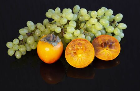Delicious Oriental fruits persimmon and a bunch of grapes on a dark glass surface.の写真素材