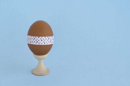 Egg standing on cup, on a soft blue background. Easter egg tied with a festive ribbon.