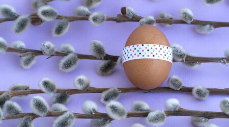 Easter egg tied with a festive ribbon, flat layout. willow branches or verbal on a light purple background, happy Easter.の写真素材