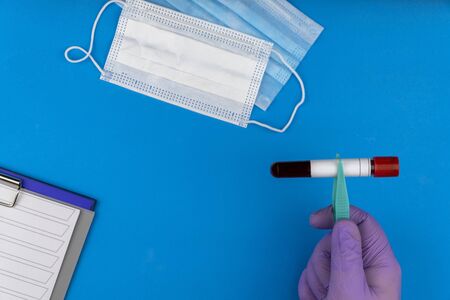 Flat lay composition with blood test tube on blue background. antiviral medical mask for protection...
