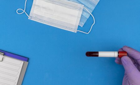 Flat lay composition with blood test tube on blue background. antiviral medical mask for protection against coronavirus COVID-19. concept of diagnosis of virus. copy spaceの写真素材