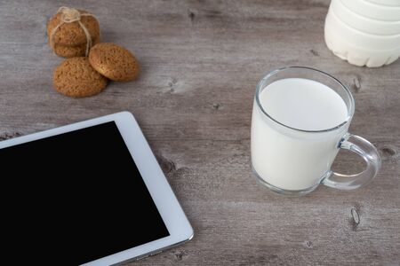 a mug of milk and croissants on a wooden background. great Breakfast in the fresh air and reading news on the gadgetの写真素材