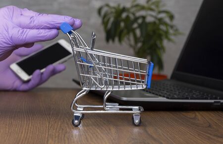 shopping cart. in the background a man orders a product on a cell phone. hands in rubber medical gloves. selective focus. online shopping.の写真素材