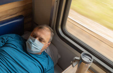 man in a medical mask near the train car. concept of travel during the pandemic. passenger is lying in his seat in the compartment of the carの写真素材