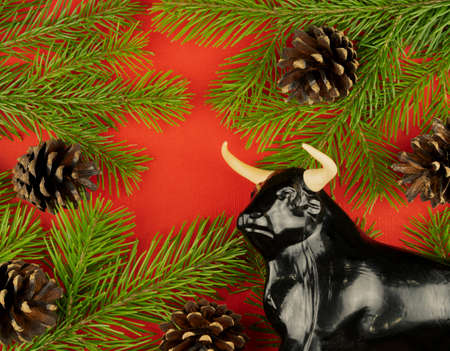 statuette of a bull on a Christmas red background. selective focus. festive decorations and fir...