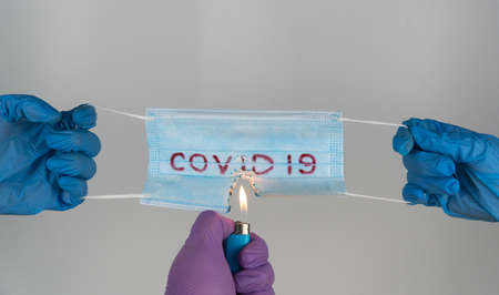 medical mask with the inscription covid-19 burns with fire. set fire to the surgical mask, destroy...