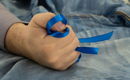 blue ribbon is clenched in his fist, the man holds the ribbon in his hand. Awareness ribbon about prostate cancer problems. Men Healthcare and World cancer day conceptの写真素材