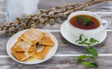 delicious cookies with condensed milk and black tea with mint. selective focus. light breakfast is served on a wooden table. porcelain cup with tonic mint tea. decorated with pussy willow.の写真素材