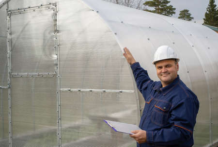 worker stands against the background of a hothouse. design and construction of polycarbonate greenhouses. male engineer installs hotbed for growing vegetablesの写真素材