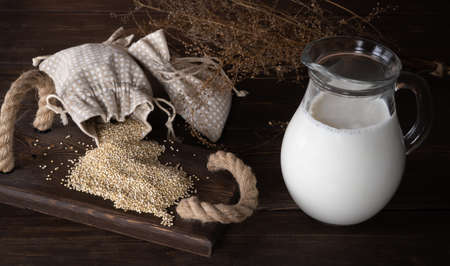 scattered quinoa grains and a jug of milk on a wooden table. Chenopodium quinoa. milk from quinoa. flexitarian drink, protein shake. natural complex of minerals and vitamins.の写真素材