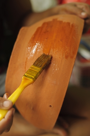 Wet orange paint on a baked clay, with a hand, holding a paint brush の写真素材