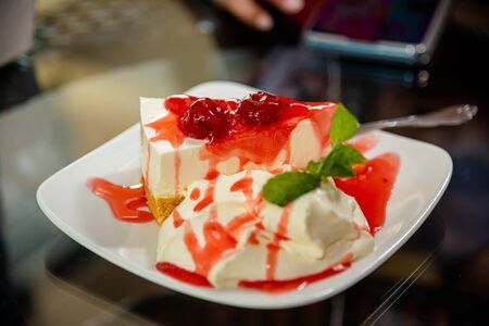 Sweet dessert with strawberry sauce decorated on a white plate on a glass tableの写真素材