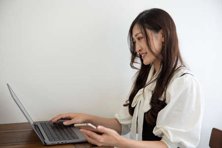 A Japanese woman checking smartphone by remote work in the small officeの写真素材