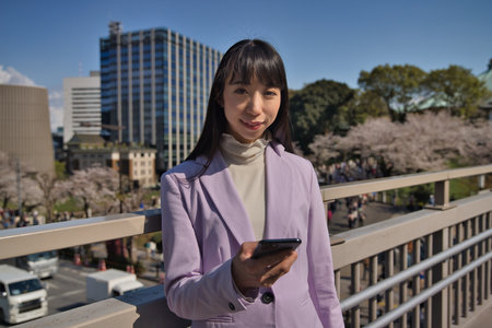 A portrait of Japanese woman with smartphone behind cherry blossomの写真素材