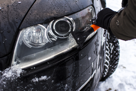 car, winter, people and vehicle concept - close-up of a man, cleans a car from snow, headlampの写真素材