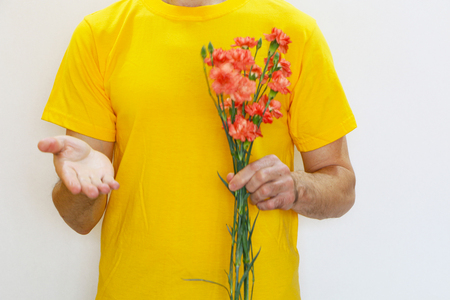 Close-up - a man in a yellow T-shirt holds carnation flowers in his hand and stretches his other hand palm upの写真素材