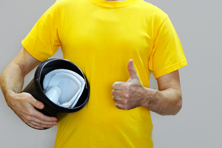 Close-up - a man in a yellow T-shirt throws a plastic powder in the trash canの写真素材