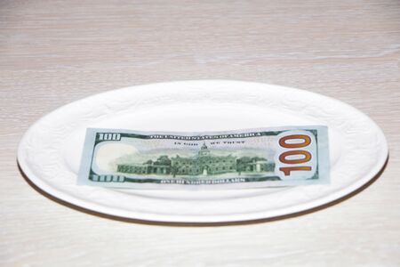 Close-up - money is lying on a white plate. Businessman is sitting at the table with fork and knife. White background.の写真素材