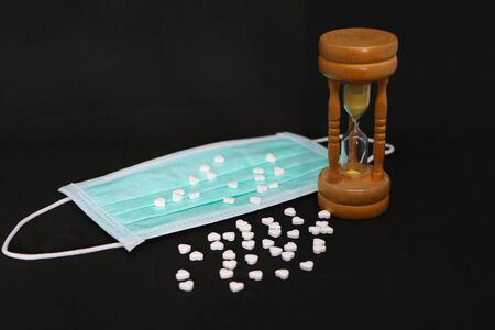 Concept - close-up of a medical mask, pills and hourglass on a black background.