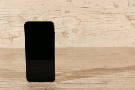 Smartphone with blank screen and modern frameless design, vertically on wooden background.