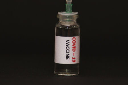 The concept of combating the coronavirus Covid-19. On a black background, a jar with a vaccine and a syringe. Concept: disease, medicine, science.の写真素材
